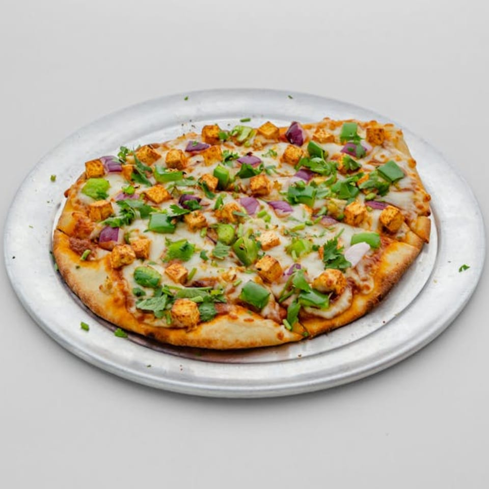 A Pizza Bites paneer pizza with green peppers, red onions, and cilantro on a metal tray.