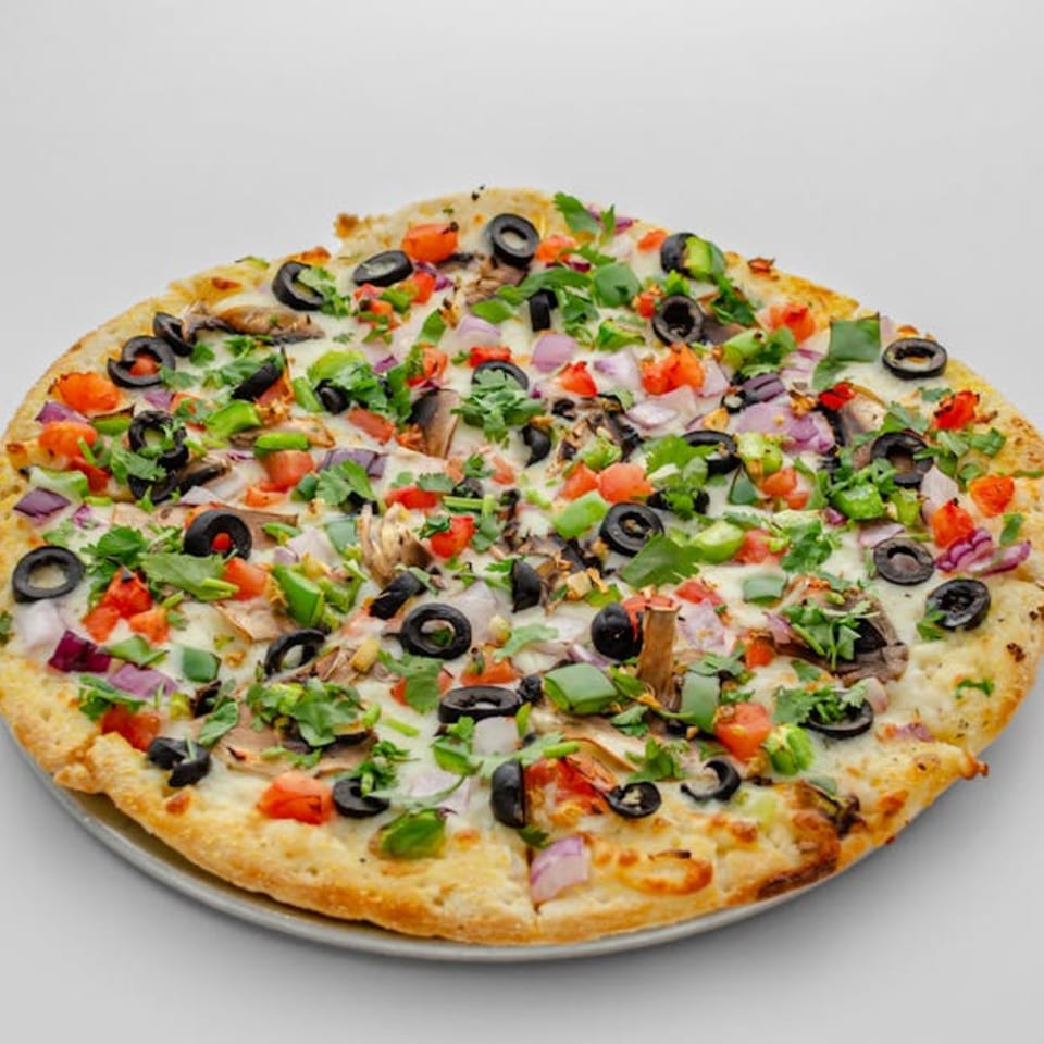 A Pizza Bites pizza with olives, tomatoes, onions, green peppers, and cilantro on a white background.