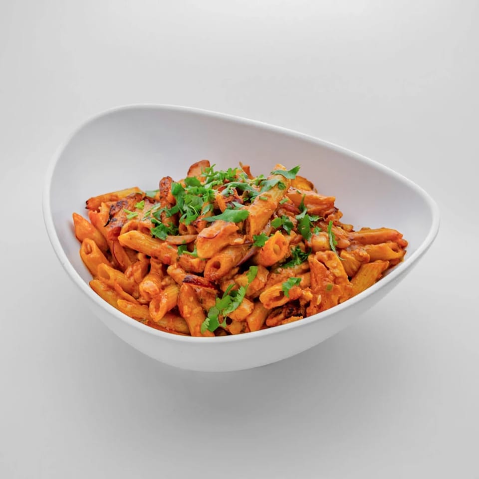 Penne pasta with red sauce and fresh green herbs in a white bowl.