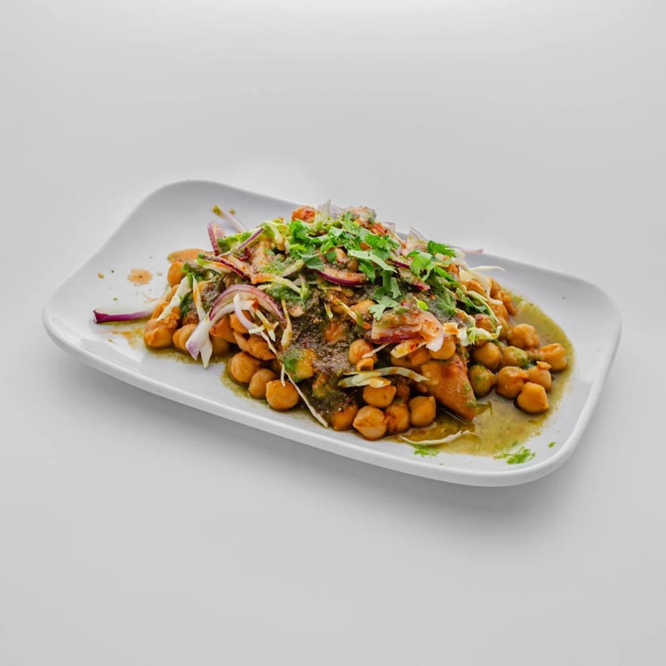 Chana chaat, a chickpea salad with onions, cilantro, and green sauce, on a white plate.
