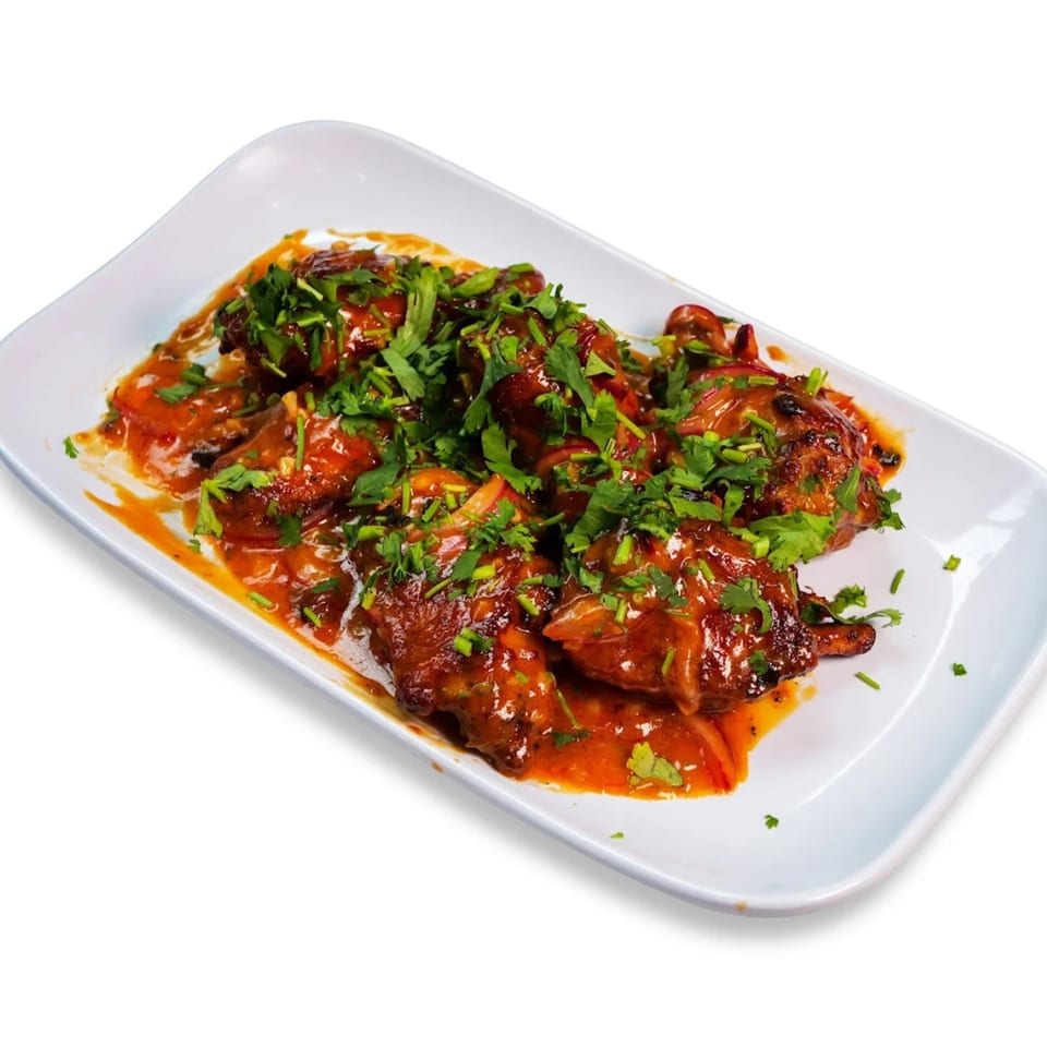 Chicken wings in a rich orange sauce, garnished with fresh green herbs on a white rectangular plate.
