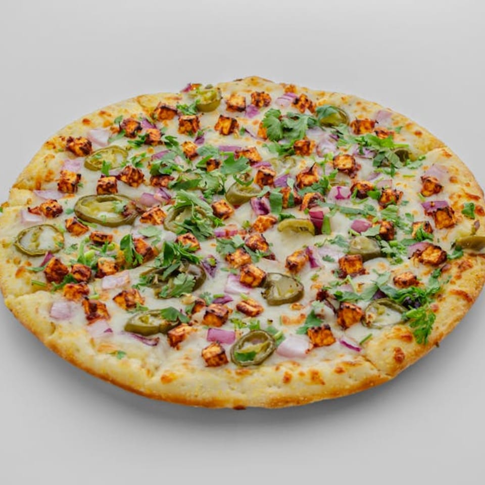 A Pizza Bites pizza topped with paneer, red onions, jalapeños, and cilantro.