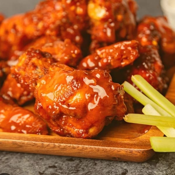 Close-up of Pizza Bites' spicy chicken wings with celery sticks on a wooden board.