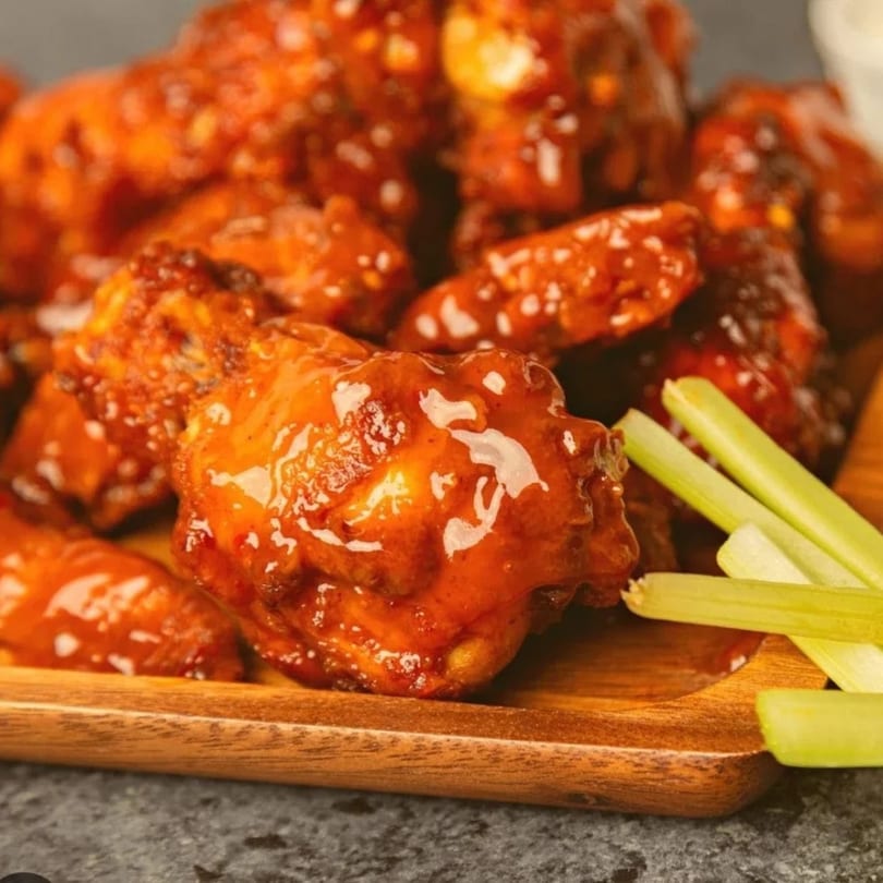 Close-up of Pizza Bites' spicy chicken wings with celery sticks on a wooden board.
